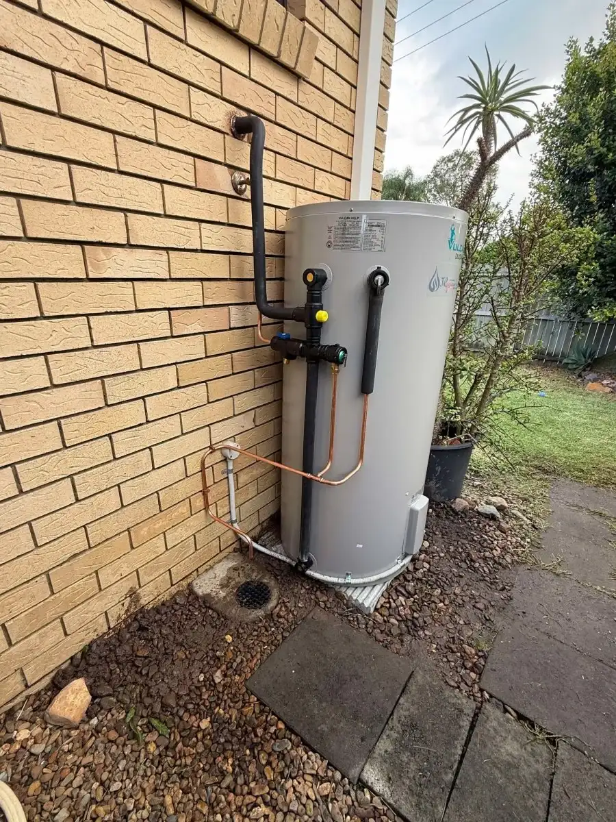 Electric hot water system installed against the exterior brick wall of a home