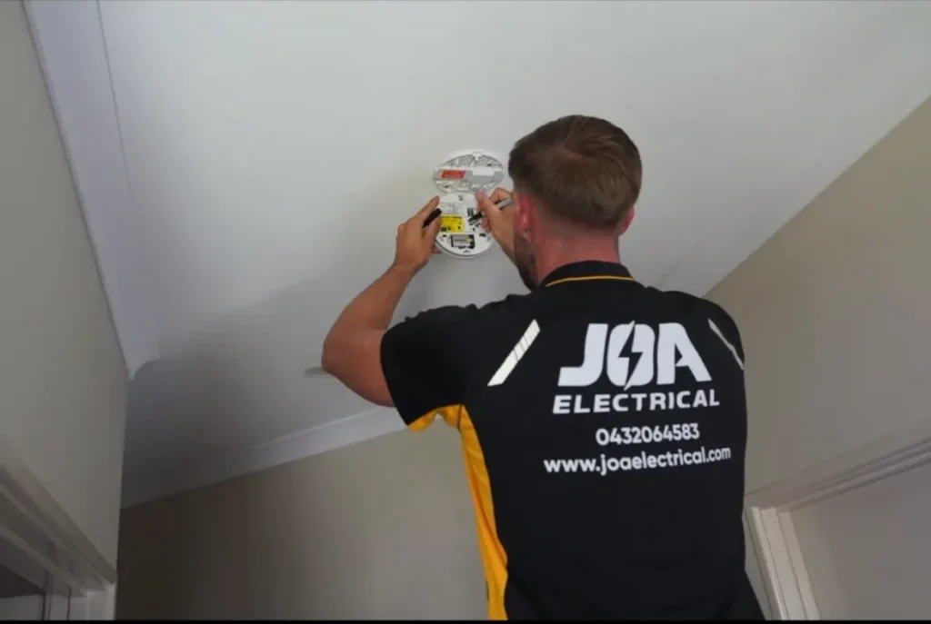 JOA Electrical electrician installing a hardwired smoke alarm on a ceiling